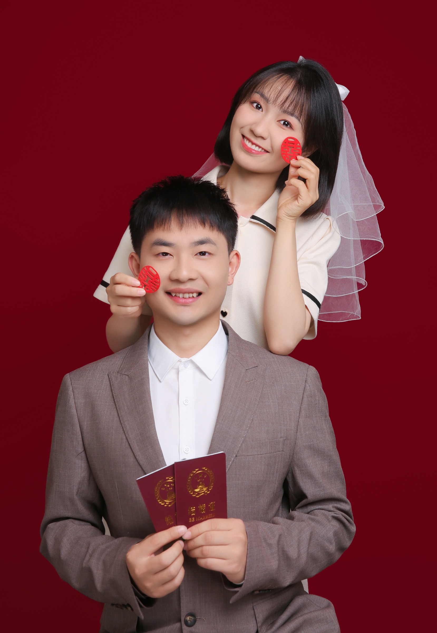 两个人在红色背景前拿着结婚证合影